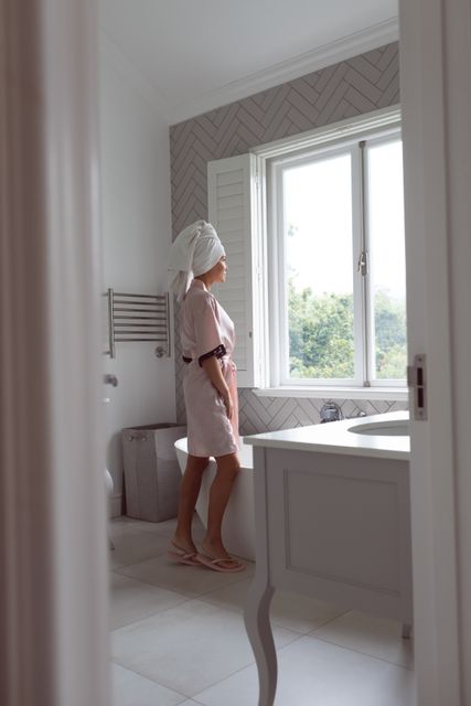 Beautiful woman standing while looking outside the window in bathroom at home