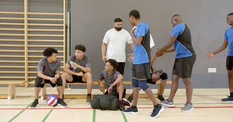 Diverse male volleyball team and coach talking on bench in indoor gym demonstrating teamwork
