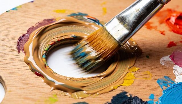 Mixing brown paint on wooden palette with brush creating glossy color textures