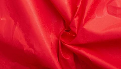 Glossy red satin fabric twisting into rosette knot close-up texture background