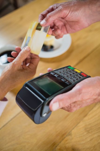 Senior woman holding a credit card while making a payment at a café. The image shows a close-up of hands during the transaction with a POS terminal. Ideal for illustrating concepts related to modern payment methods, senior lifestyle, customer service, and retail transactions. Useful for financial services, technology, and lifestyle content.