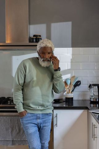 Senior african american man leaning on counter talking on smartphone in modern kitchen
