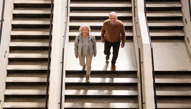 Senior Couple Ascending Modern Atrium Staircase, Active Retirement, Urban Mobility