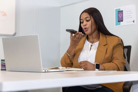 African american woman speaking into smartphone during virtual meeting at modern desk