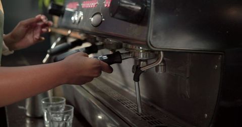 Barista attaching portafilter to commercial espresso machine, closeup hands and steam wand