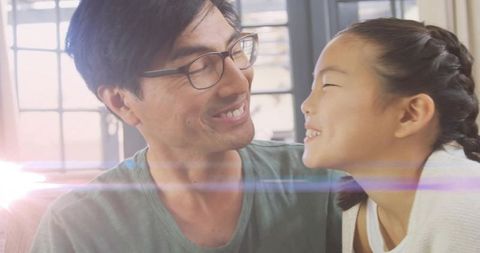 Asian father and daughter sharing sunlit moment on couch with warm lens flare