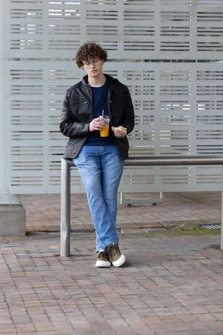 Teen leaning on transit shelter rail holding orange juice and sandwich urban commuter moment