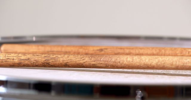 Close-up view of two wooden drumsticks resting on a snare drum, emphasizing the texture and detail of the sticks and drum. Useful for content related to music education, drumming tutorials, band promotional materials, and articles on rhythm and percussion instruments.