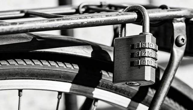Hanging three-dial combination lock on urban bicycle rack closeup showing tire, spokes, metal textur