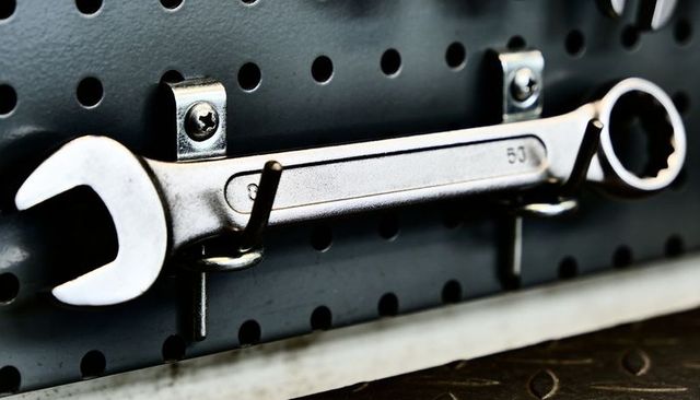 Chrome combination wrench hanging on perforated pegboard closeup workshop tool detail