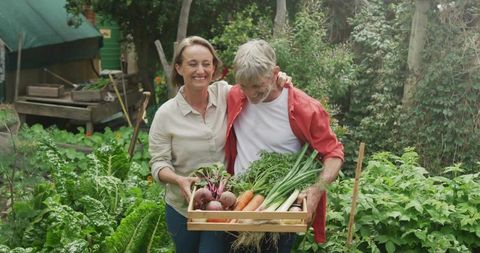 Happy Couple Holding Freshly Harvested Vegetables in Backyard Garden