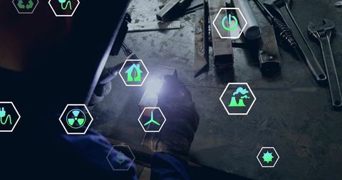 Woman welding at metal bench with augmented reality energy and sustainability icons
