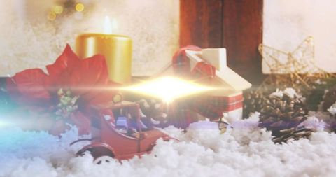 Vintage red toy car in snowy holiday display with wrapped gift, candlelight and poinsettia
