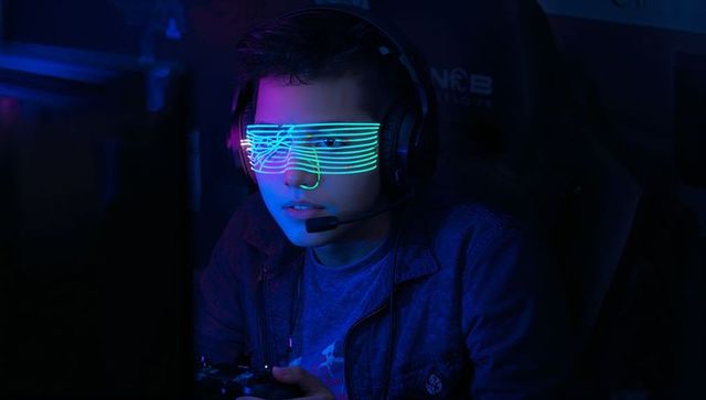 Young gamer wearing led shutter glasses playing controller in neon esports streaming setup