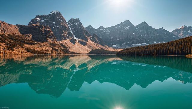 Reflecting turquoise glacial lake mirroring jagged snowcapped peaks and evergreen forest