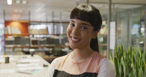 Smiling young professional standing at modern office desk with greenery and scattered papers