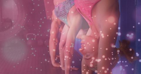 Trio balancing on handstands against studio wall with pink bokeh lights and padded mat