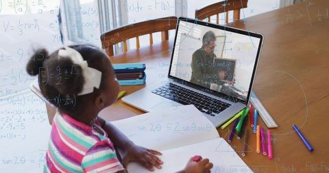 Child studying math online with tutor on laptop at dining table doing homework