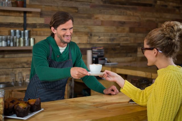 Smiling male barista serving coffee to female customer in cafe