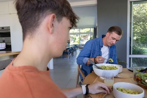 Father and teenage son sharing pasta at modern kitchen table, casual family mealtime