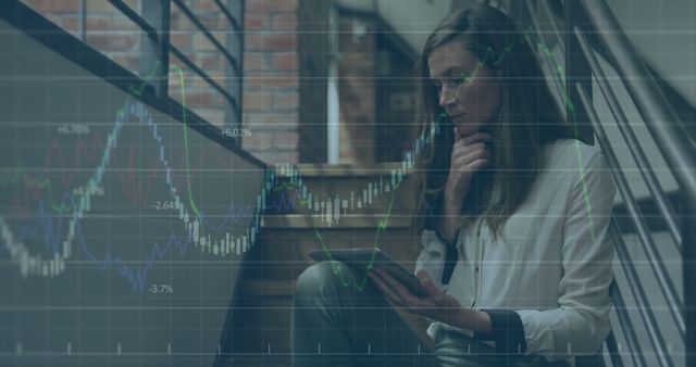 A businesswoman sits in an industrial-style office, analyzing stock market data on a digital tablet with overlaid graphs. Ideal for use in financial and business-related materials, investment guides, technology content, or articles discussing market trends and economic analysis.