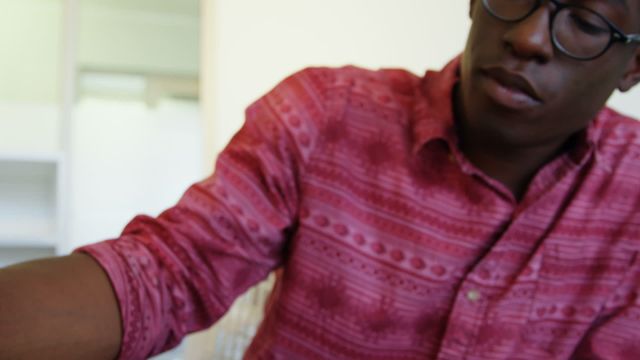 An African American male graphic designer is immersed in his work, using a graphic tablet in a modern office setting. The atmosphere is one of focus and creativity, ideal for project-based freelancers or remote workers. This image is perfect for illustrating concepts related to creative work environments, productivity, diversity in the tech industry, and remote working solutions.