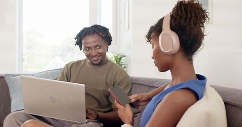 African American Couple Relaxing on Couch Using Laptop and Smartphone with Headphones