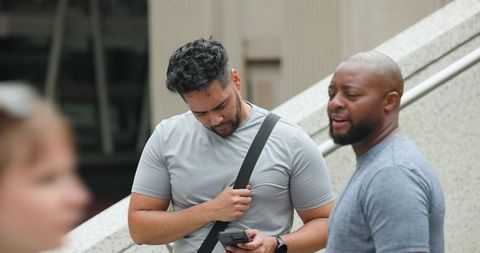 Men checking smartphone on urban stairway, casual conversation in city plaza