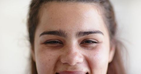 Smiling young woman closeup showing freckles and bold eyebrows, natural beauty portrait