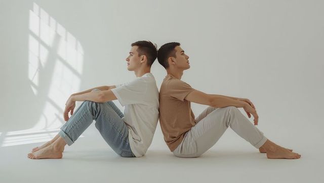Minimalist portrait showing two asian men sitting back-to-back in sunlit neutral studio