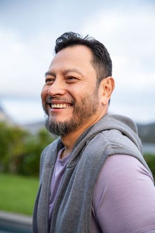 Mature asian man smiling by lake wearing gray hoodie and purple shirt