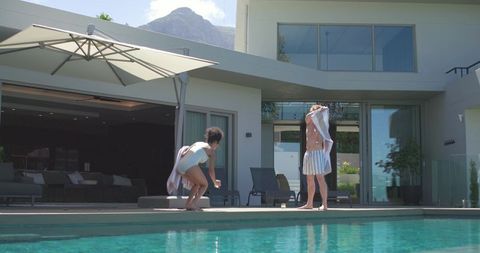 Couple drying off by modern poolside with umbrella and patio seating, woman crouching