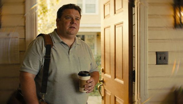 Man leaving home holding coffee cup and carrying leather messenger bag at front door