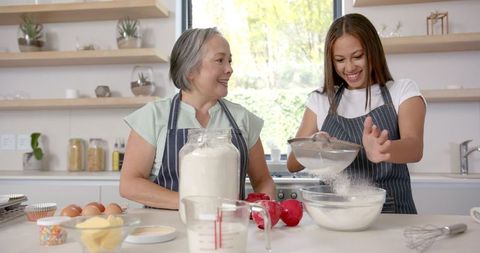 Asian grandmother and granddaughter baking together in cozy kitchen