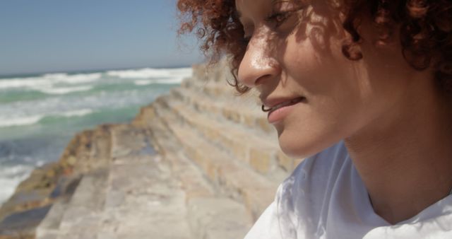 Biracial woman sitting on stone stairs and looking down with copy space on sunny beach. Feminity, summer, vacations and free time, unaltered.