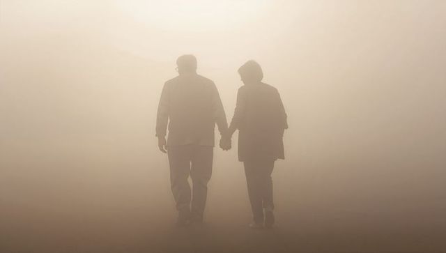 Senior couple walking hand in hand through soft fog toward bright light, silhouetted