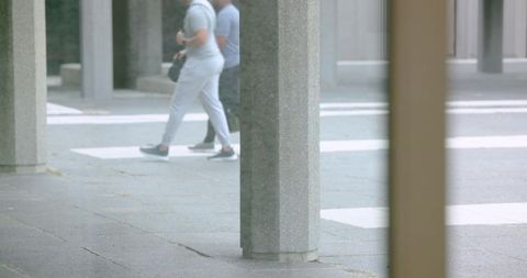 Urban pedestrians crossing plaza past concrete columns in muted overcast colonnade