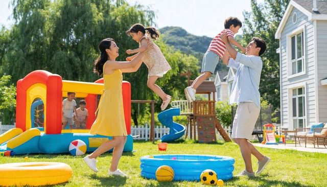 Joyful family playing in backyard with bounce house, kiddie pool and playset on sunny summer day