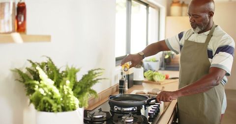 Mature man cooking, pouring oil in modern kitchen