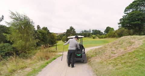 Golfer retrieving club from cart on scenic fairway