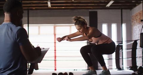 Woman Performing Squat Jump in Industrial Gym with Personal Trainer