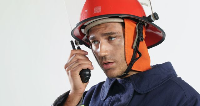 Biracial male firefighter wearing hardhat, protecting suit and talking on walkie-talkie, copy space. Fire prevention, professionals, safety, technology and communication concept, unaltered.