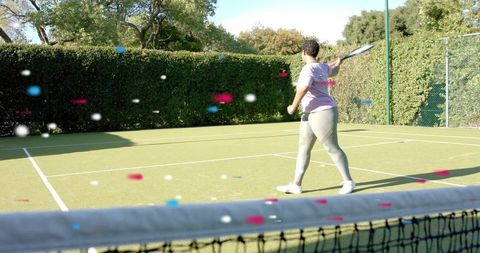 Athletic woman swinging racket on sunny outdoor tennis turf with hedge backdrop near net