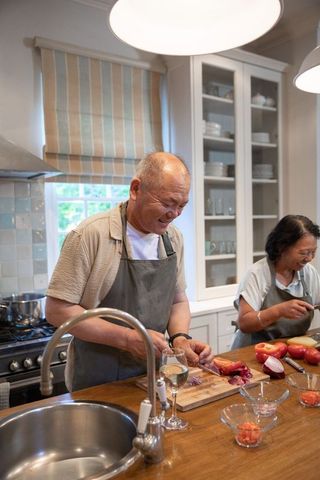 Chinese couple smiling and chopping tomatoes and onions on wooden kitchen island with wine
