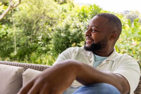 African american man relaxing on patio sofa smiling, casual outdoor leisure