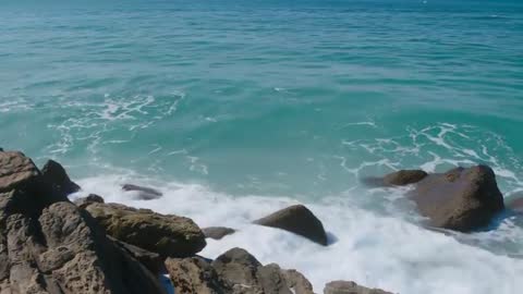 Waves crashing and receding over rocky coastline with turquoise surf and spray