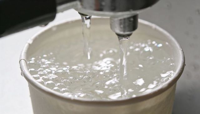 Filling paper cup with clear water from dual metal spouts, bubbles and ripples