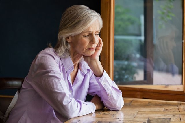 Sad senior woman sitting at table in cafe shop