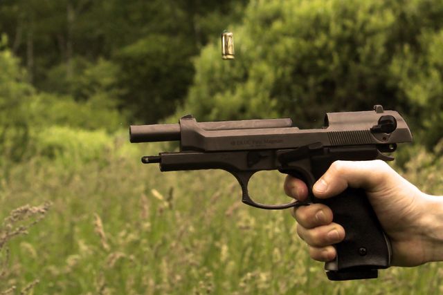 Hand holding and firing a pistol outdoors in a grassy field, with a bullet captured in mid-air. Great for topics related to firearms, shooting sports, safety training, or self-defense. Can be used in articles, educational materials, or promotional content for shooting ranges or safety equipment.