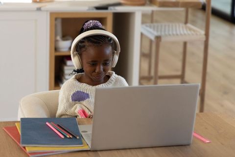 African american girl studying online with headphones on laptop at home